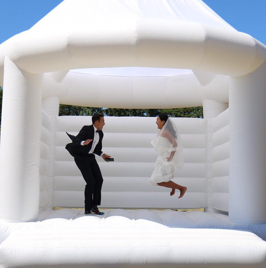 married couple bouncing in a white wedding castle